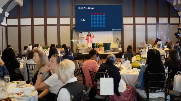 Suzanne Knight delivering the keynote at the Dare to Dream conference, with a slide behind her showing that women hold a significant percentage of leadership positions.