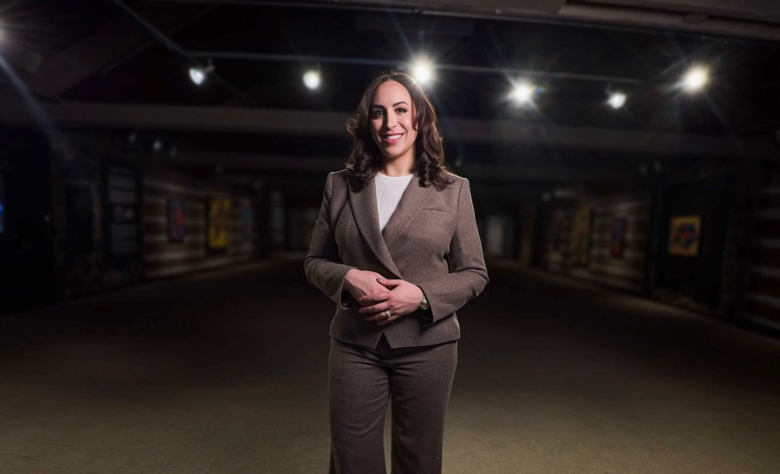 Suzanne Knight, global keynote speaker and consultant, standing in a suit with lights behind her