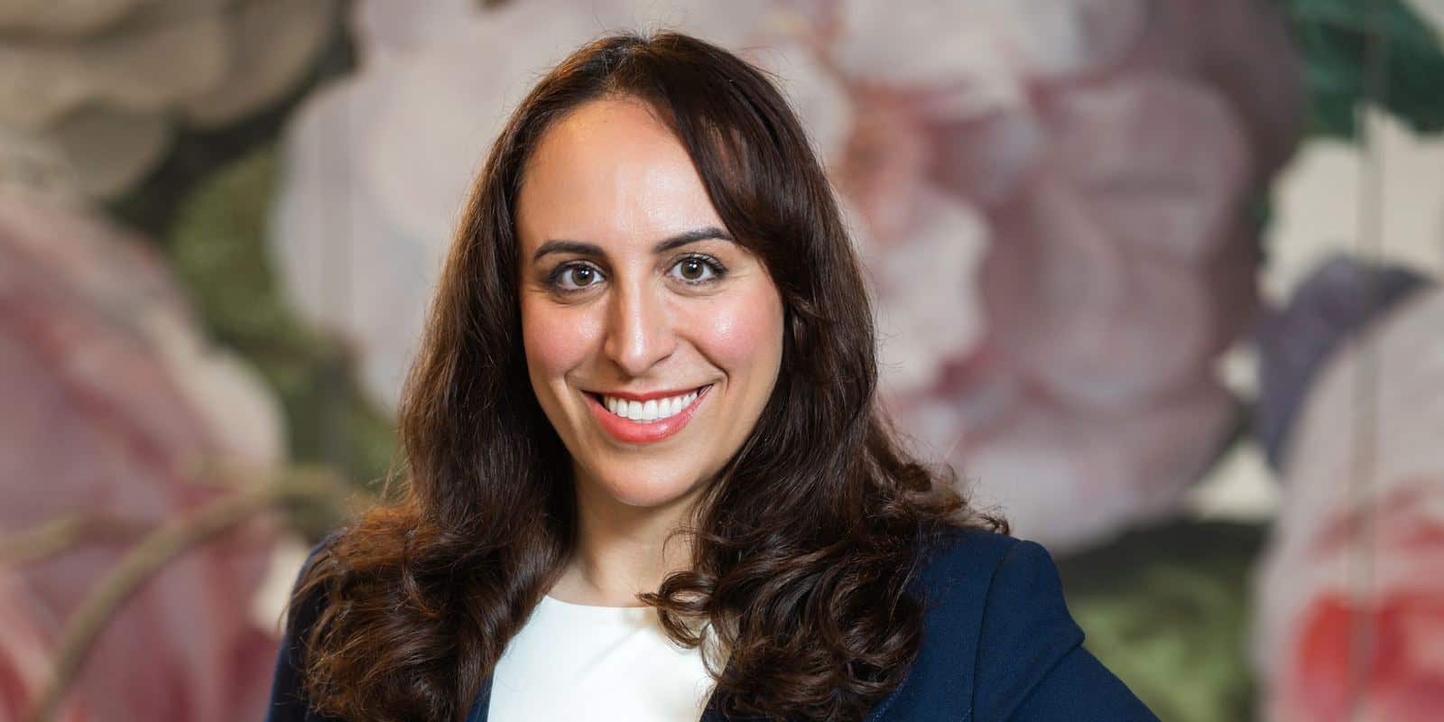 Portrait of Suzanne Knight smiling in a navy blazer against a floral wall
