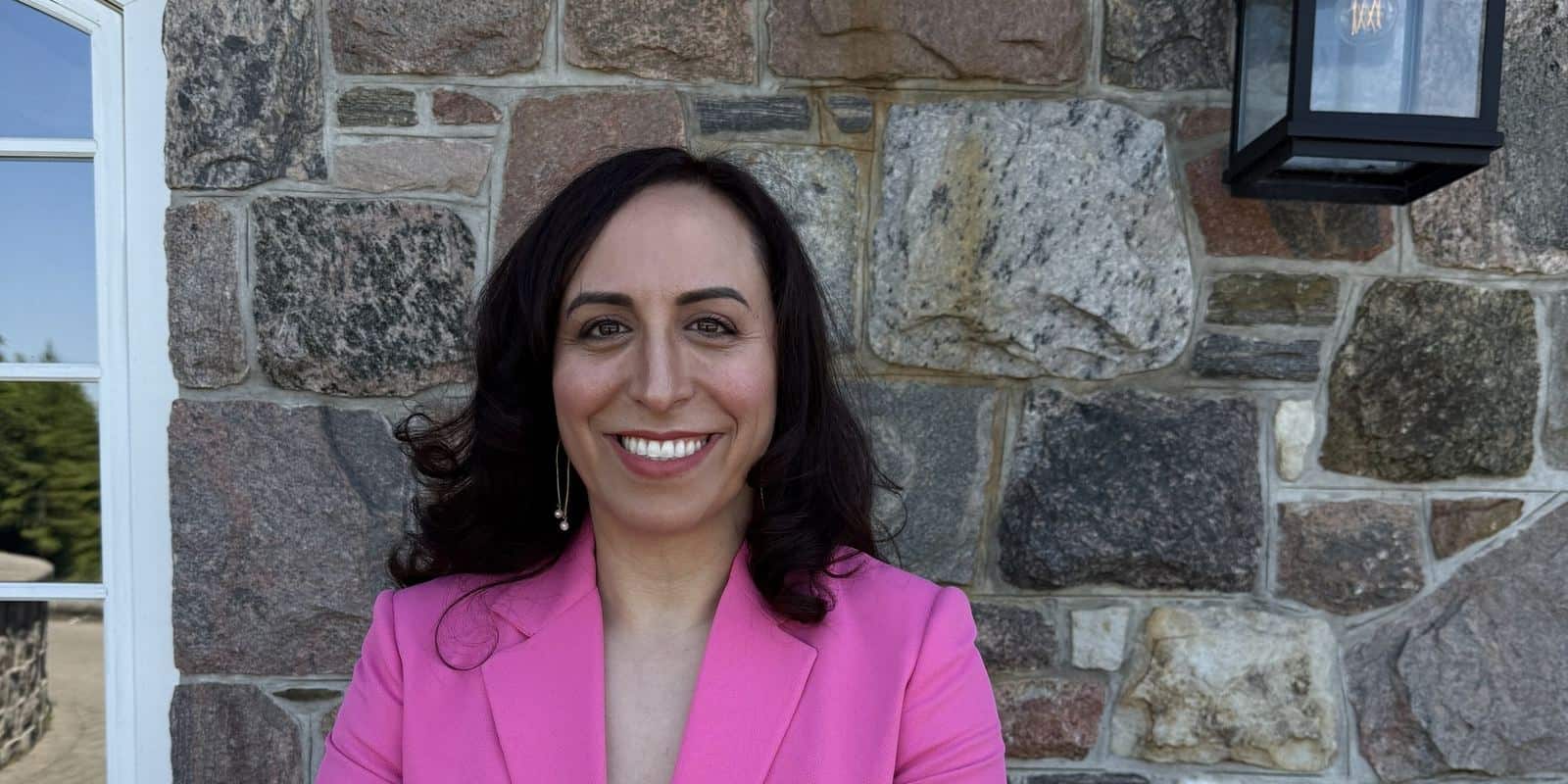 Portrait of Suzanne Knight smiling in a pink blazer against a stone wall