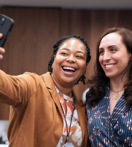 Suzanne Knight speaking at a conference with a smiling attendee taking a selfie.